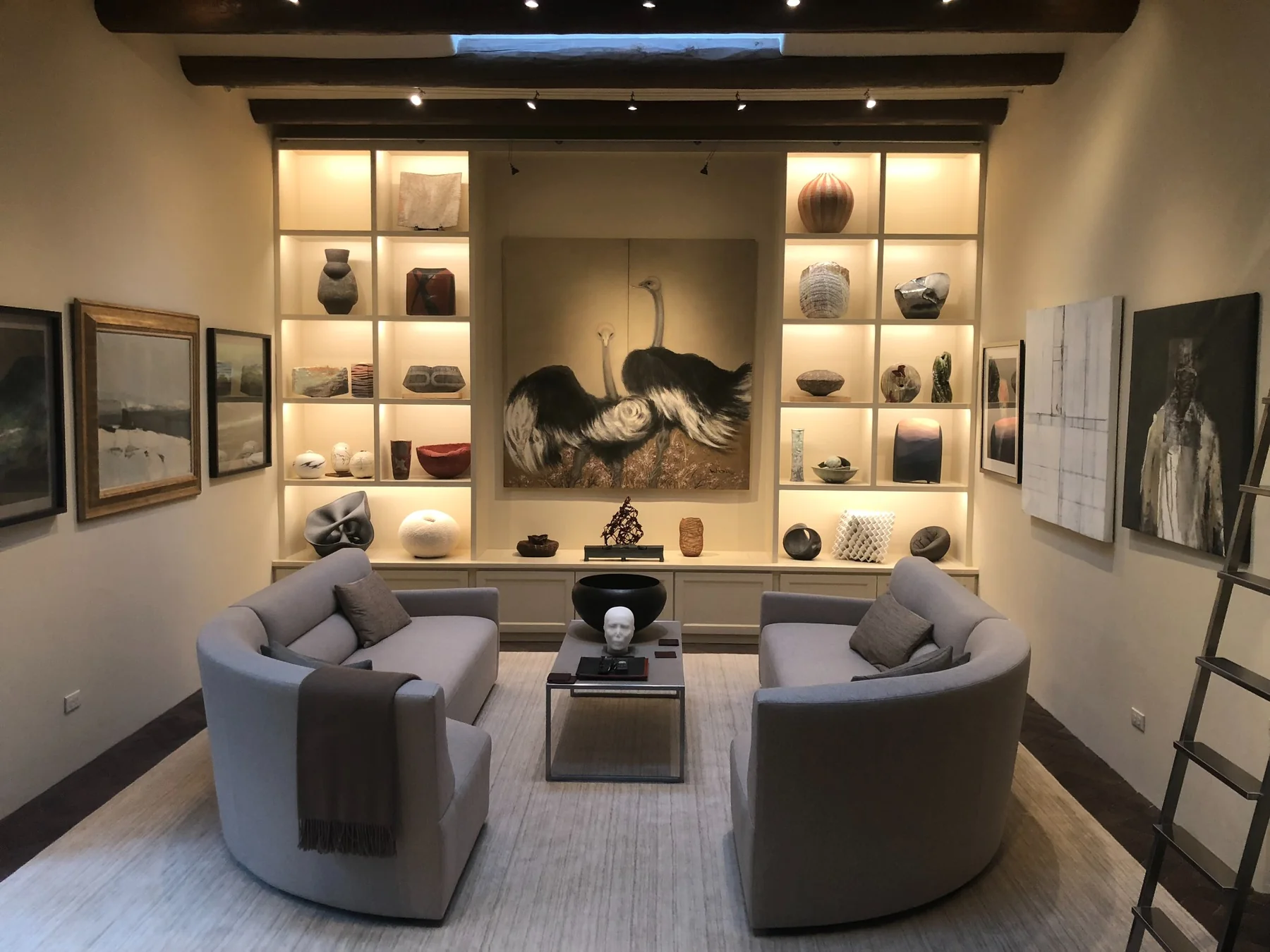 Santa Fe art-filled sitting room with built-in illuminated shelves, ceramics, sculpture, and a large painting